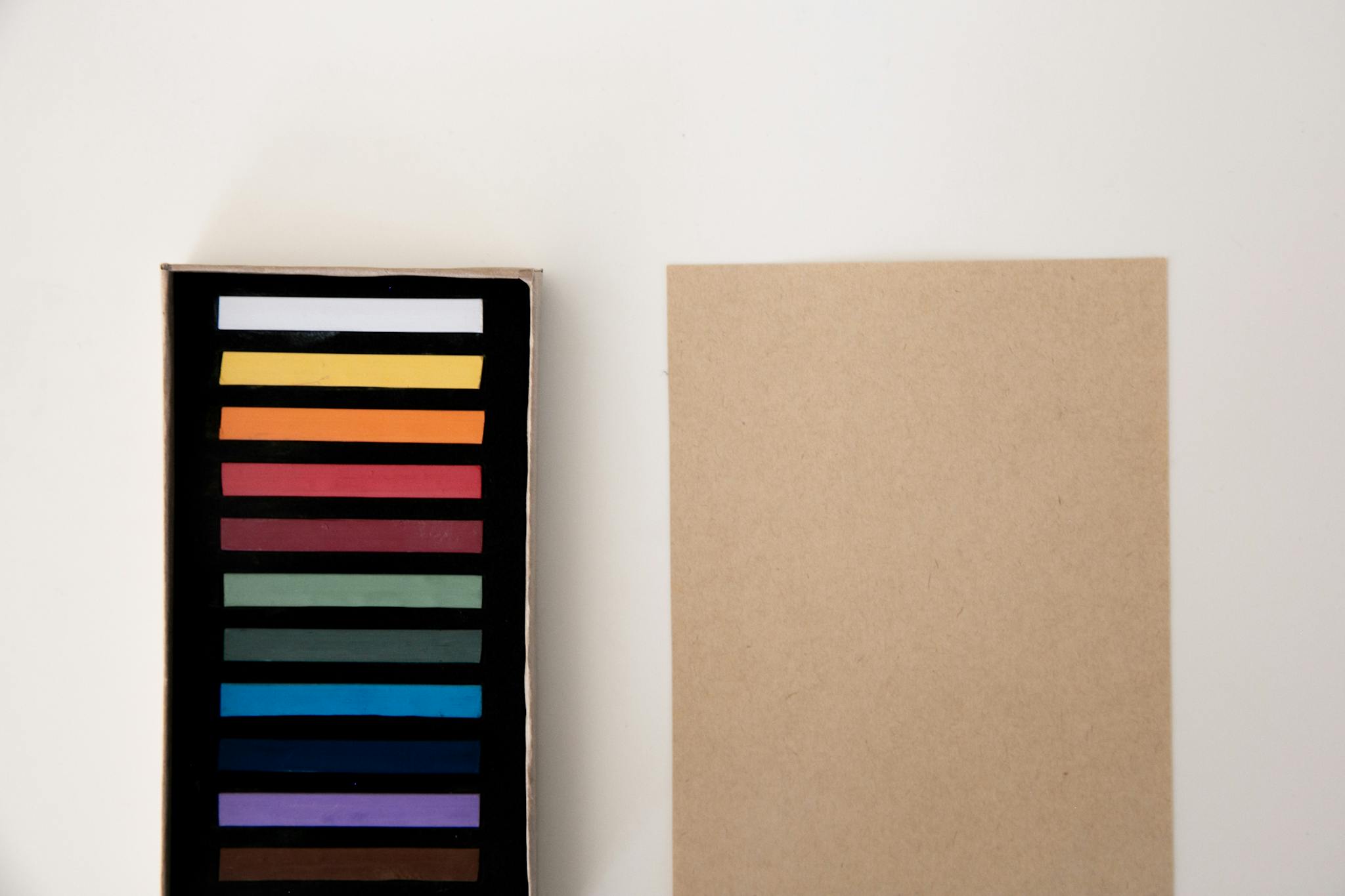 A box of colorful pastel sticks alongside a blank sheet on a white background, perfect for creative projects.