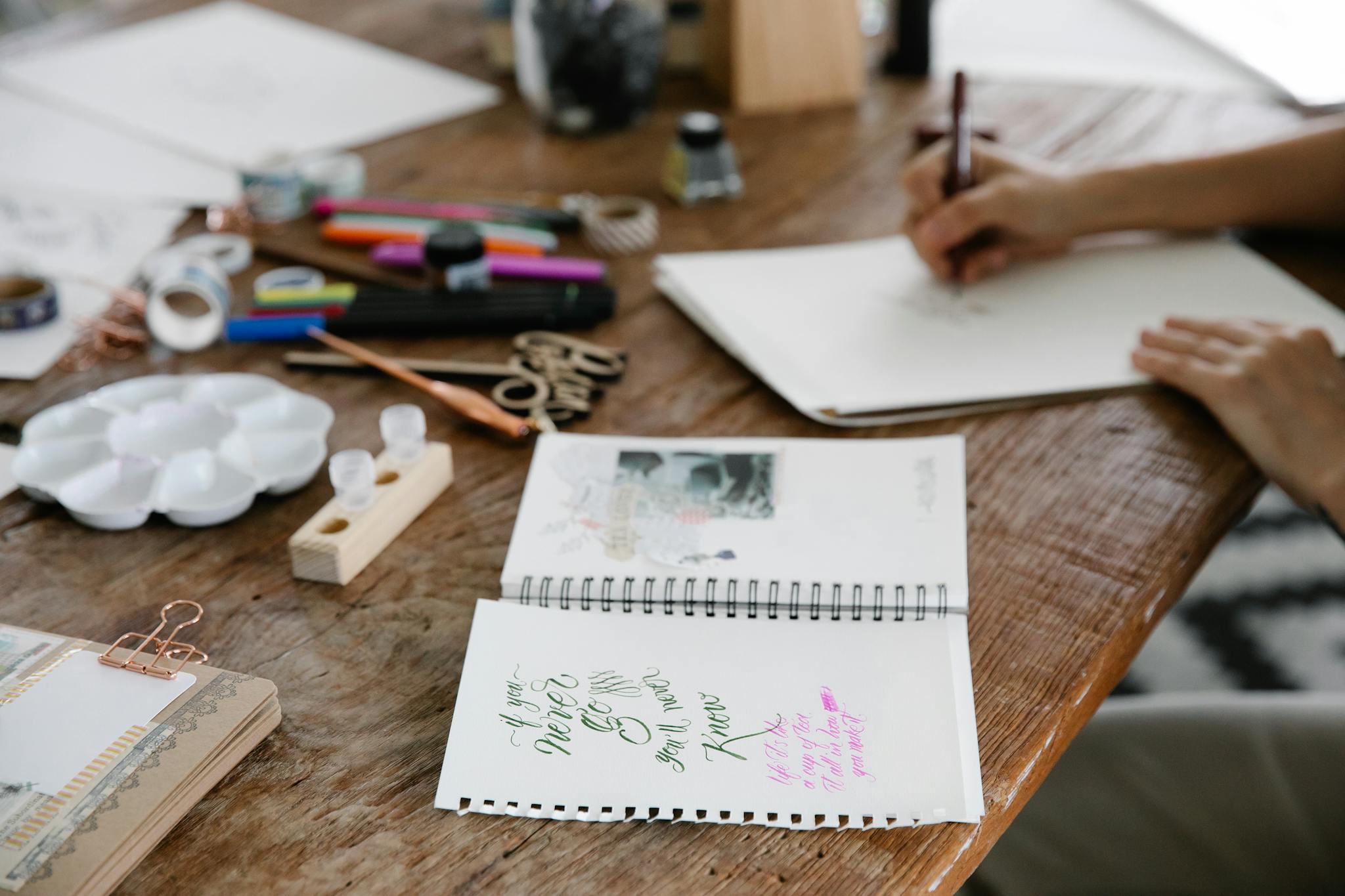 A wooden table filled with art supplies and sketches, showcasing creative work in progress.